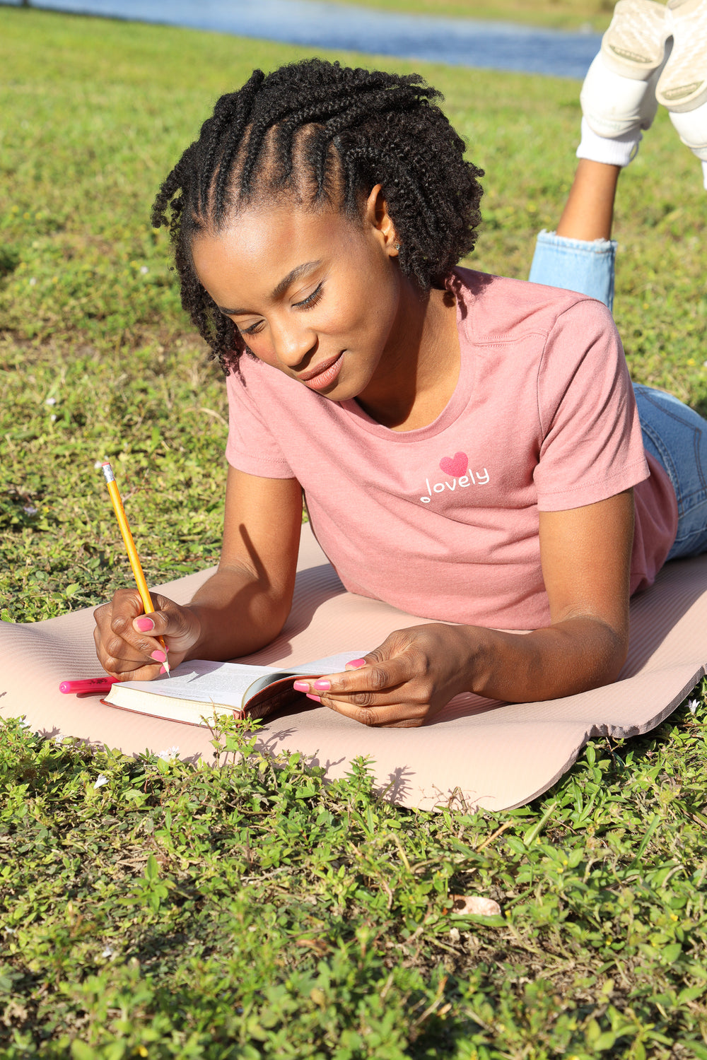 Person lying on grass writing in a notebook with a pencil